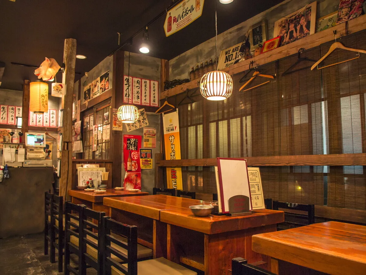 手羽市本千葉店の店内。木のテーブル席と提灯の明かり、壁に貼られたポスター